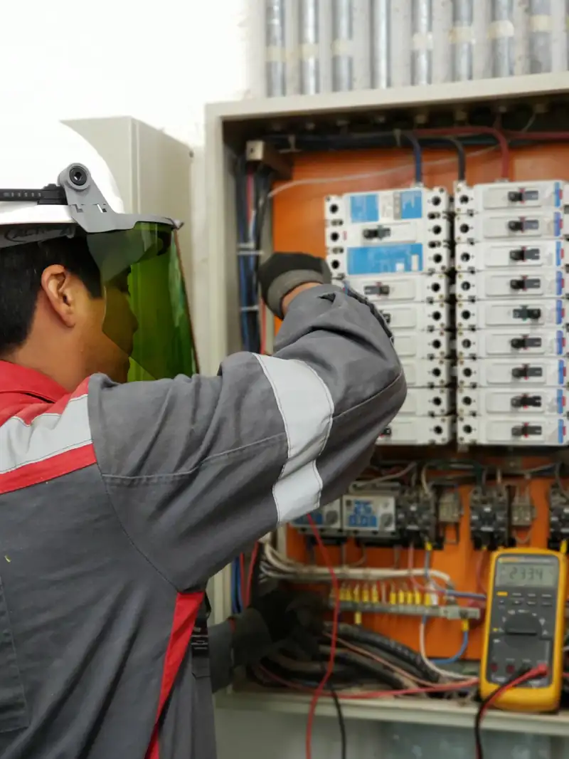 Electrician with protective gear testing an electrical panel